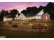 Elegant home with a brick facade, lush landscaping, and warm exterior lighting against a vibrant sunset sky at 228 Indian Creek Rd, Locust Grove, GA 30248