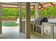 View of covered outdoor kitchen with stainless steel cabinets and a grill overlooking the pool at 405 Highgrove Dr, Fayetteville, GA 30215