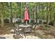 Charming outdoor dining area with stone patio, table, chairs, and a bright red umbrella amidst a lush green garden setting at 100 Rosemont, Peachtree City, GA 30269