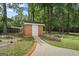 Brick shed with a white door surrounded by manicured landscaping and mulch beds in a wooded yard at 171 Ponderosa Drive, Fayetteville, GA 30214