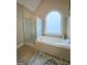 Bright bathroom featuring a tiled tub, separate glass shower, and a large arched window at 110 Vicarage Ct, Johns Creek, GA 30005
