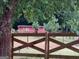 A red barn is seen from behind a wooden fence surrounded by lush foliage at 2585 Old Jackson Rd, Locust Grove, GA 30248