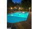 The pool has a dark gray concrete base and the blue water is shimmering beneath the illumination of night time lighting at 604 Clearwater Ct, Mcdonough, GA 30252