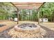 Outdoor stone fire pit set beneath a pergola, surrounded by mature trees and landscaped rocks at 70 Summer Walk Dr, Covington, GA 30016