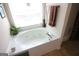 Inviting corner bathtub with jets, bright windows, and neutral tile flooring at 300 Cloverwood Dr, Fayetteville, GA 30215