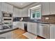 Close up of kitchen features white cabinetry, stainless steel appliances, dark backsplash, and hardwood floors at 1214 Weatherstone Way, Peachtree City, GA 30269
