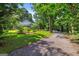 View of the blue exterior and gravel driveway, framed by towering trees and a well-manicured lawn at 7550 Fielder Rd, Jonesboro, GA 30236