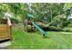 A view of the backyard with a wooden playset and slide on a lush green lawn surrounded by mature trees and landscape at 1486 Maple Ridge Dr, Suwanee, GA 30024