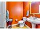 Unique half bathroom featuring a vibrant orange wall, pedestal sink, and a decorative mirror at 1373 Fall River Dr, Conyers, GA 30013