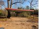 Image shows a carport with a red roof, metal beams and concrete pad surrounded by a treed lot at 5700 Miles Rd, South Fulton, GA 30349
