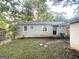 A backyard view of a single-story home with a small patio, black door, green trash bin, and unkempt yard at 1901 Clarke Ln, Decatur, GA 30035