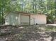 Large white outbuilding with a roll-up door nestled among tall trees in a rustic setting at 224 Potts Se Rd, Conyers, GA 30094
