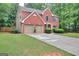 Brick home with a two-car garage surrounded by a well-maintained lawn and mature trees offering curb appeal at 5765 Woodstone Dr, Cumming, GA 30028