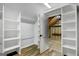 Open closet with white shelving units and wood floors, looking into unfinished attic space at 1572 Hines Rd, Moreland, GA 30259