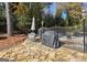 Stone patio featuring an outdoor dining set, grill, and privacy fence, surrounded by mature trees at 2119 Pine Heights Ne Dr, Atlanta, GA 30324