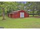 Exterior view of a red metal barn with a white roof and doors, nestled on a lush green lawn with mature trees at 435 Jackson St, Locust Grove, GA 30248