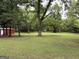 Large green yard with mature trees and partial view of a red outbuilding at 435 Jackson St, Locust Grove, GA 30248