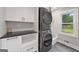 Modern laundry room with gray stacked washer and dryer, white cabinets, and tiled floor at 2885 Laurel Green Ct, Roswell, GA 30076