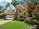 Beautiful two-story brick home featuring an attached garage, mature trees, and lush green lawn at 1504 Oglethorpe Dr, Suwanee, GA 30024