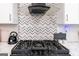A kitchen cooktop with a stylish backsplash, stainless steel vent hood, and modern appliances at 5490 Bent Grass Way, Douglasville, GA 30135