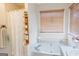 Corner tub with tile surround, wooden shelving unit, and window with blinds at 402 Stonebrooke Dr, Auburn, GA 30011