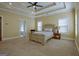 Bright, carpeted main bedroom with a large window, tray ceiling, and a doorway to the bathroom at 100 Clydesdale Ct, Tyrone, GA 30290