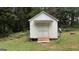 A white shed with double doors nestled in a wooded backyard provides extra storage at 10 Stagg Trce, Social Circle, GA 30025