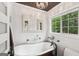 White-themed bathroom with an elegant bathtub, modern chandelier and a window view at 10875 Shagbark Trl, Roswell, GA 30075