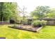 Landscaped backyard showcasing a well-maintained lawn, mature trees, and a wooden garden plot with newly planted trees at 30 Carolyn Ct, Social Circle, GA 30025