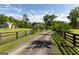 A long private driveway passes a red building, mature trees, lush green lawns, and black fencing at 110 Green Meadow Ln, Fayetteville, GA 30215