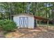 White wooden shed with double doors, covered storage space, and surrounded by lush greenery at 130 Emerald Dr, Mcdonough, GA 30253