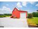 View of red barn with a white garage door and gravel driveway surrounded by green grass on a sunny day at 385 Liberty Church Rd, Carrollton, GA 30116