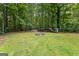 Backyard featuring a fire pit, stacked wood, green grass, and surrounding trees at 205 N Strathmore Dr, Sharpsburg, GA 30277