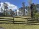 Landscaped front yard featuring a rustic wooden fence, grassy lawn, and a line of trees against a sunny, blue sky at 2534 Highway 155 N, Mcdonough, GA 30252