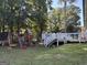 Large backyard with a wooden playset, deck, and a lush green lawn surrounded by mature trees at 517 Pebble Pt, Loganville, GA 30052