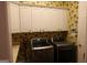Functional laundry room with white cabinets, floral wallpaper, and stainless steel washer and dryer at 433 Abbey Springs Way, Mcdonough, GA 30253