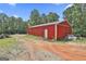 Exterior view of a red barn surrounded by trees with a dirt driveway at 6220 Petersburg Rd, Fairburn, GA 30213