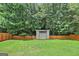 View of the backyard shed surrounded by a wooded yard with a wooden privacy fence at 147 Calico Loop, Grantville, GA 30220