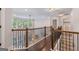 Upstairs hallway with hardwood floors and railing overlooking a living room with many windows at 2307 Loughridge Dr, Buford, GA 30519