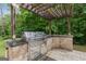 Stone-clad outdoor kitchen featuring stainless steel grill, sink and countertop space under a pergola at 2307 Loughridge Dr, Buford, GA 30519