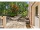 Backyard view of a brick home, a stone patio, landscaping, and a pathway leading into the wooded area at 3088 Hidden Falls Dr, Buford, GA 30519