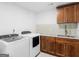 A modern laundry room with a washer and dryer next to a sink with a tile backsplash and wood cabinets at 2775 Club Valley Ct, Jonesboro, GA 30236