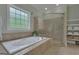 Bright bathroom featuring a bathtub with jets and a glass-enclosed shower, complemented by neutral tile and towel storage at 185 Platinum Ridge Pt, Fayetteville, GA 30215