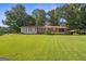 Ranch home with brick and vinyl siding, red metal roof, manicured lawn, and mature shade trees at 6674 Cowan Mill Rd, Winston, GA 30187