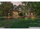 Charming stone home featuring a lush front yard with mature trees and manicured landscaping at twilight at 914 Champions Way, Mcdonough, GA 30252