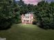 Aerial view of a traditional brick home with a well-manicured lawn, mature trees, and decorative balcony at sunset at 100 Castlebrook Chase, Tyrone, GA 30290