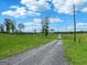 Gravel driveway leading to a sprawling green property with mature trees under a sunny, blue sky at 357 Old Driver Rd, Whitesburg, GA 30185
