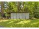View of a metal storage shed with double doors and a shaded overhang in the backyard with garden space at 2164 Old Rex Morrow Rd, Morrow, GA 30260