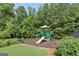 A community playground with a slide, climbing bars, and playhouse, surrounded by lush trees and landscaping at 320 Silverbell Ln, Sharpsburg, GA 30277