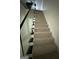 Carpeted staircase featuring a modern glass railing for safety and elegance at 6409 Caledon Ct, Locust Grove, GA 30248